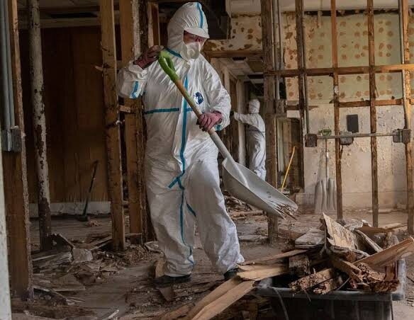 Restoration worker in protective suit clearing debris from a damaged building